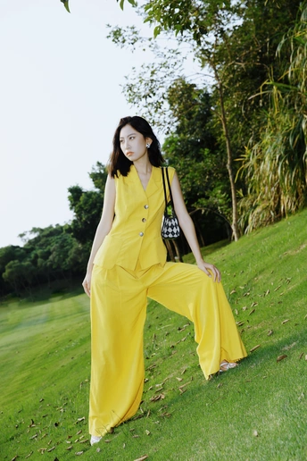一位穿着黄色连衣裙和黄色裤子的女人在草地上摆姿势