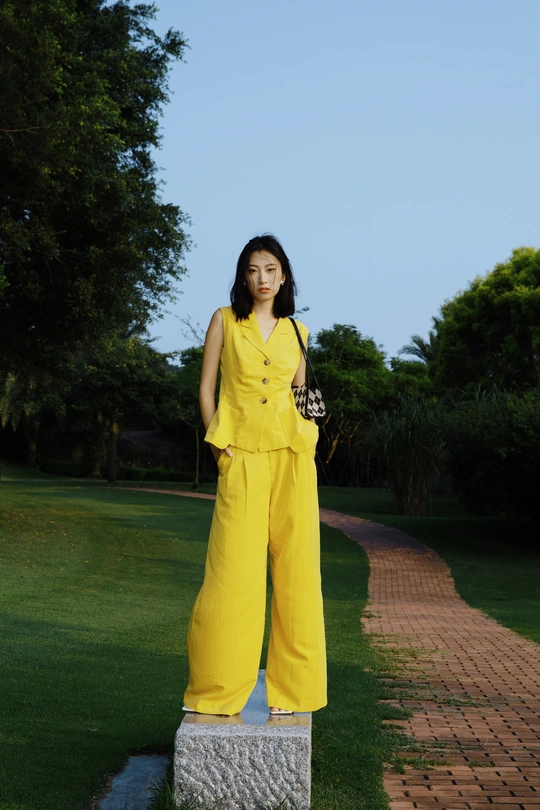 一位穿着黄色裤子黄色西装站在一座雕像旁边的女人