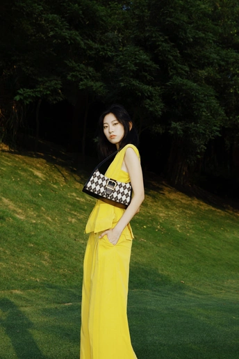 一位穿着黄色长袍的女性站在茂密的绿色背景上