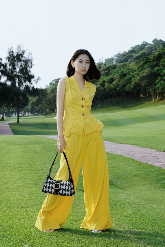 一位穿着黄色裤子和黑色包的女人在高尔夫球场上摆姿势