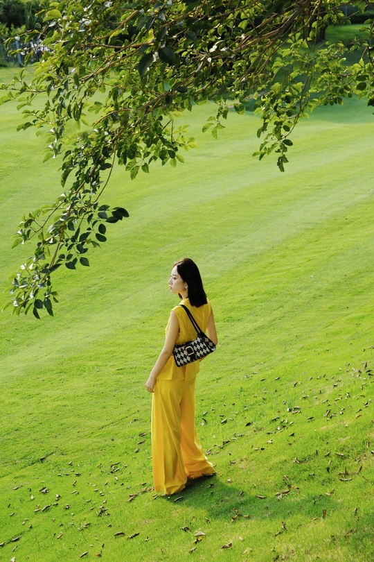 一位穿着黄色连衣裙的年轻女子站在一片绿色草地上。
