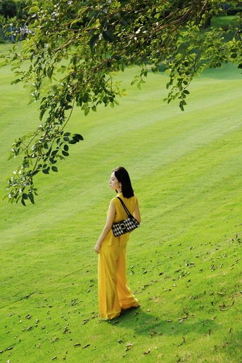 一位穿着黄色连衣裙的年轻女子站在一片绿色草地上。