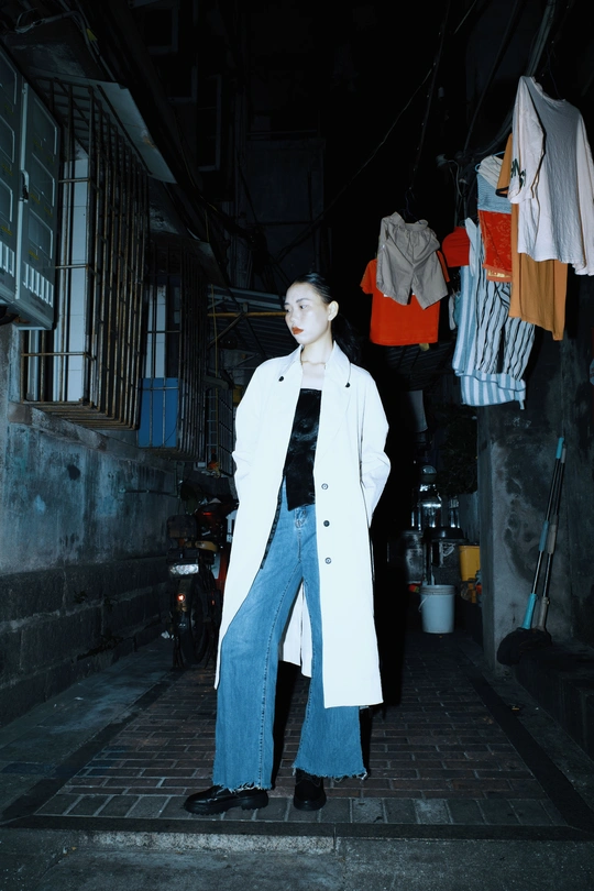 一个穿着白大褂和牛仔裤的女人站在一条黑暗的巷子里