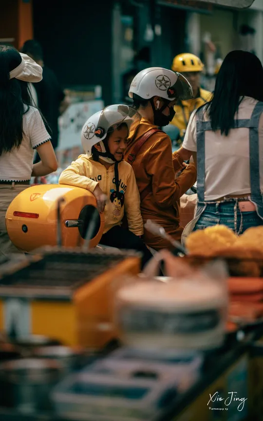 一个戴着头盔的女孩站在一辆摩托车旁边