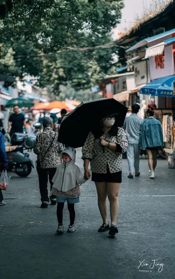 一位女士拿着黑伞 带着小女孩走在拥挤的街道上