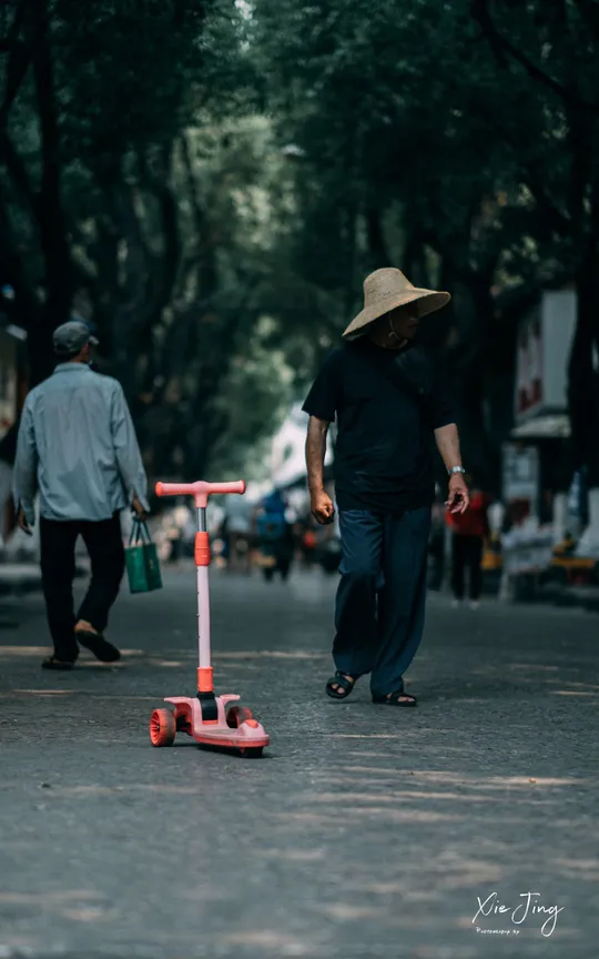 一个戴帽子的男人骑着红色的滑板车沿着街道滑行