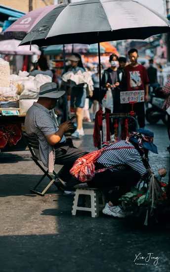 一个人坐在一把椅子上 在街市上 在其他人背景中 在伞下。