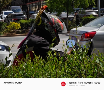 一个戴头盔的男子坐在摩托车上 摩托车停在停车场 停车场里有汽车在街上。