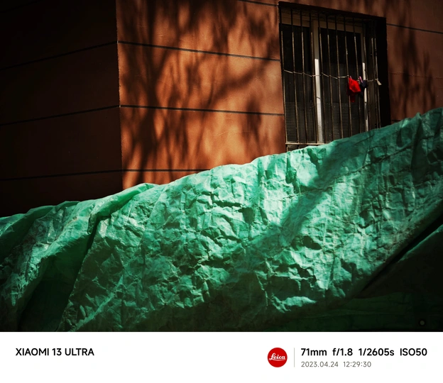 一座带有红色窗户和红色建筑物的墙壁上有阴影 并被绿色床单覆盖的房屋。