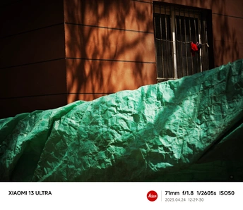 一座带有红色窗户和红色建筑物的墙壁上有阴影 并被绿色床单覆盖的房屋。