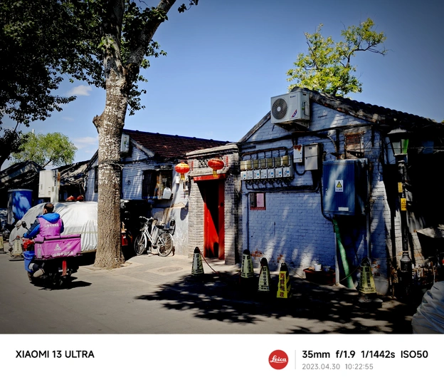 一个人骑着粉色自行车沿着一个小建筑和一棵树旁边的小街