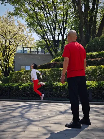 一位穿红衬衫的男子和一位穿红衬衫的女子在公园里带着一个小女孩跑。