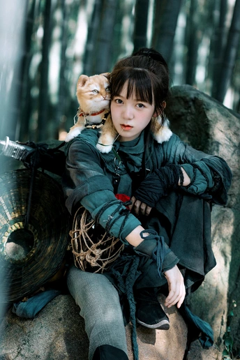 一个穿着黑色衣服的年轻女子抱着一只小猫坐在森林中的一块岩石上