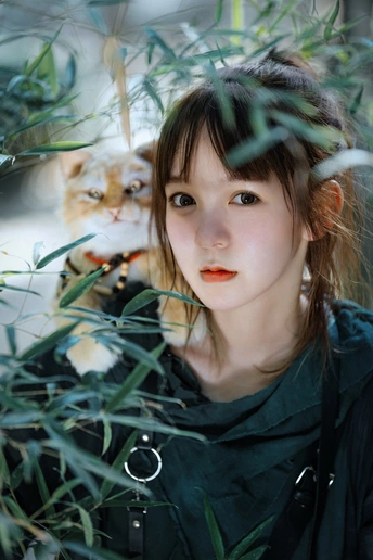 站在一株植物后面的年轻女子 一只橙色猫在灌木丛中。