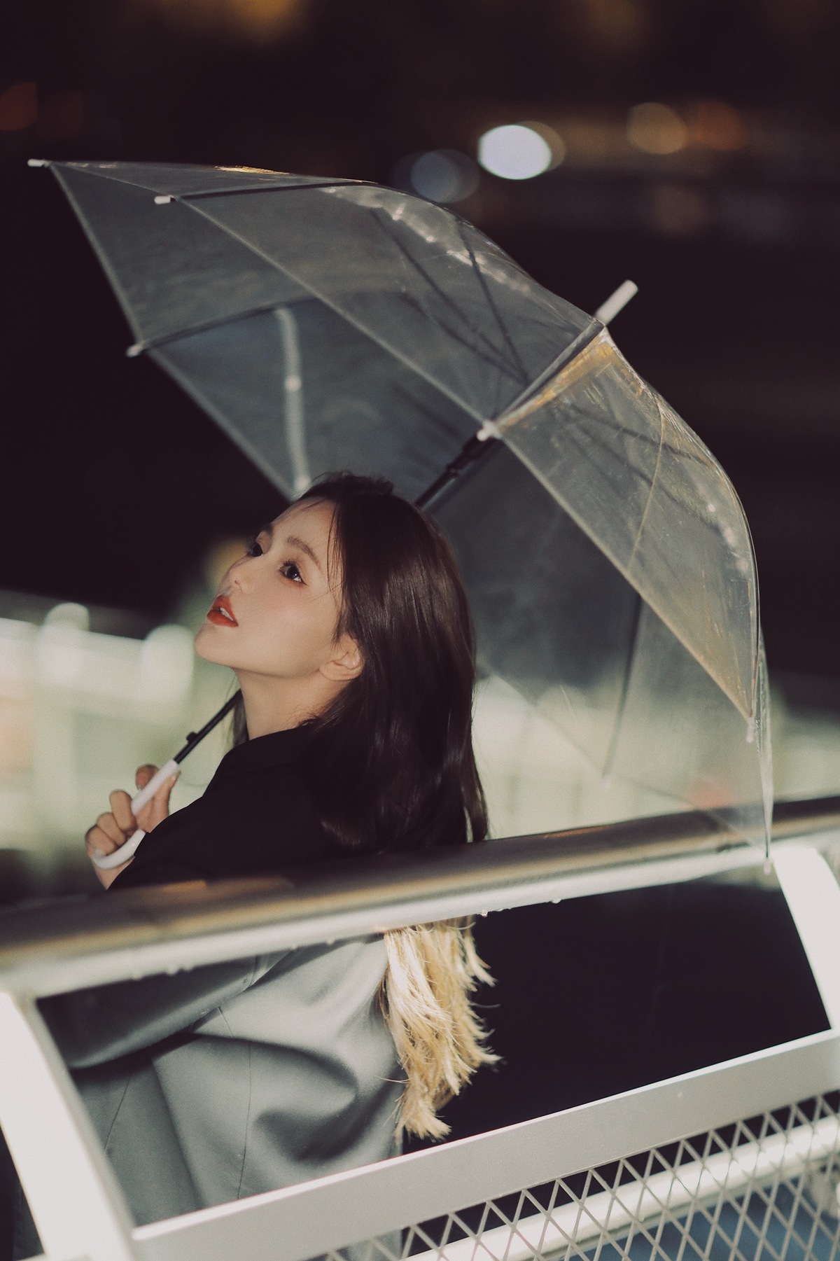 雨中夜晚站立的年轻女子手持透明雨伞