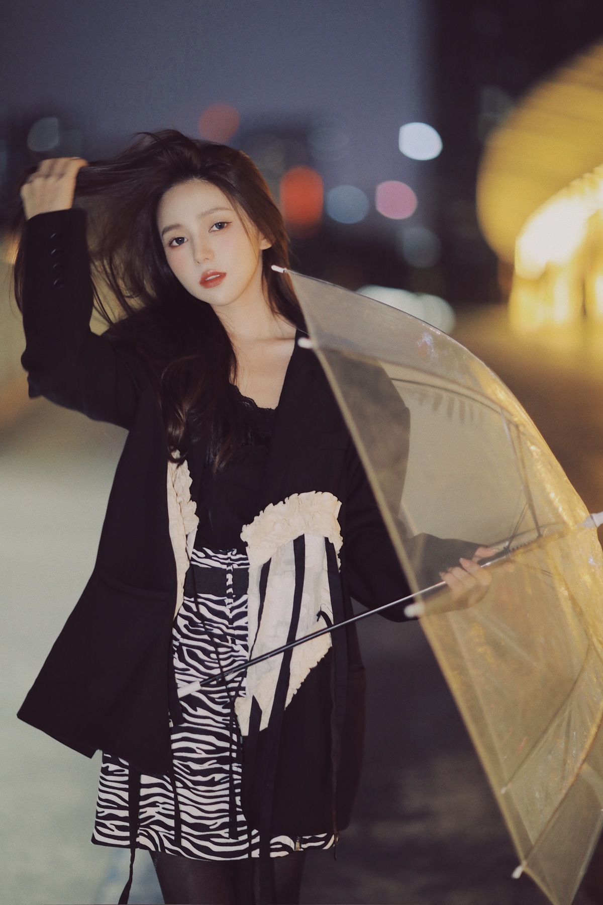 一个穿着黑白裙子的年轻女子站在夜晚的街道上 手持打开的黄色雨伞。