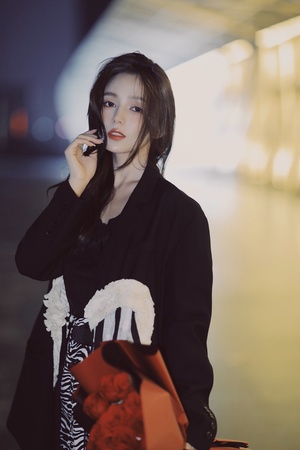 一位穿着黑色外套的年轻女子手持一个包和手机站在外面