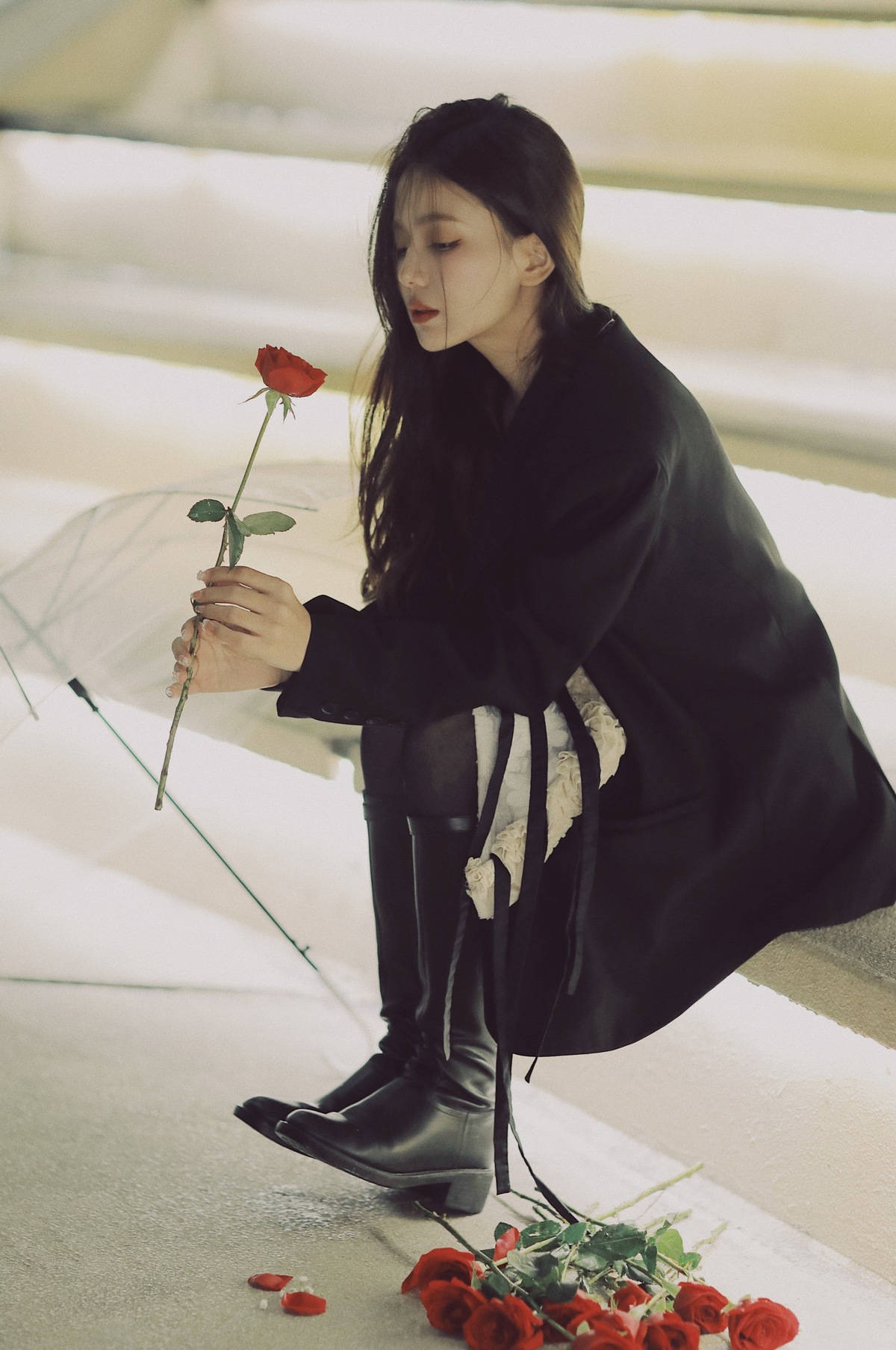 穿黑色靴子的女人手里拿着一朵红玫瑰和一把伞在地面上