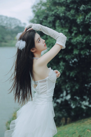 一位美丽的年轻女子穿着一件白色连衣裙 站在湖边 将她的长发披在前面。