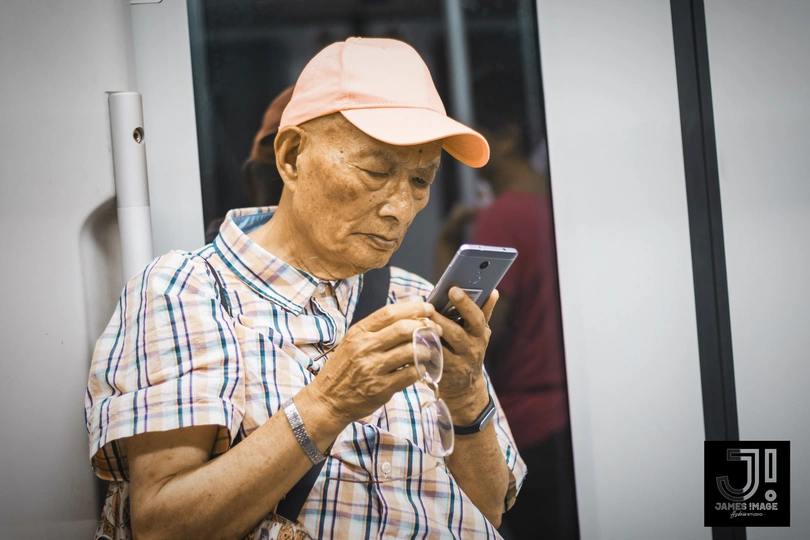 一个戴粉色帽子和格子衬衫的老男人正在看他的手机。