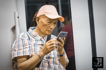 一个戴粉色帽子和格子衬衫的老男人正在看他的手机。