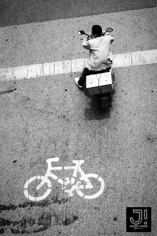 一个男子骑摩托车沿着街道行驶 路边坐着一个人。