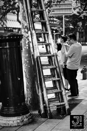 一张黑白照片 一个人靠在街边的一根杆子上 而街上的人们站在那里。