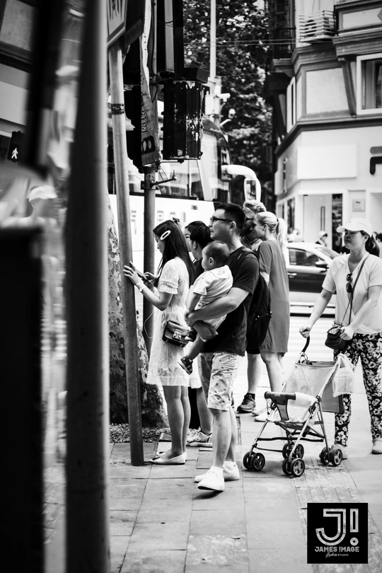 一张黑白照片 展示了一群人沿着繁忙街道的人行道行走。