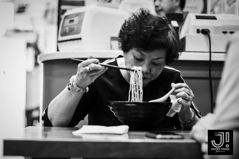 一位女性坐在桌子旁 用筷子吃一碗面条。