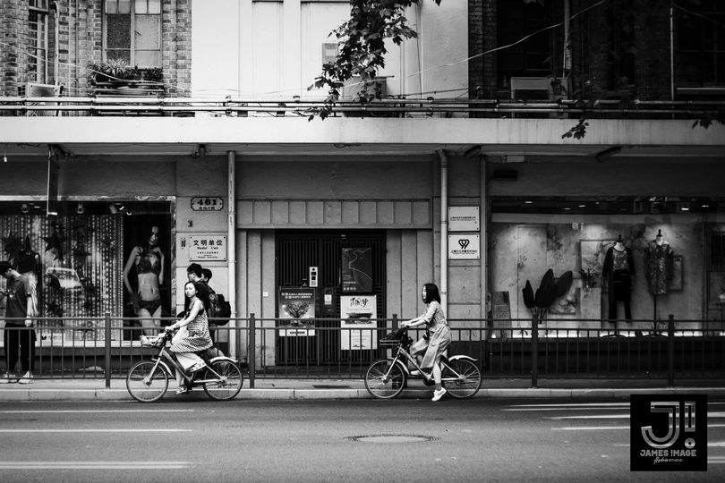 一张黑白照片 展示了城市街道上骑自行车的人和过马路的人。