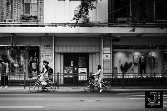 一张黑白照片 展示了城市街道上骑自行车的人和过马路的人。