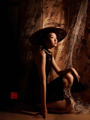 一位穿着黑色连衣裙和帽子 坐在门廊旁 有窗帘和雨伞的美丽年轻女子。