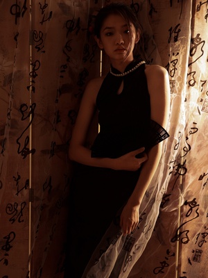 一个穿着黑色连衣裙的年轻女子站在一扇薄纱窗帘前