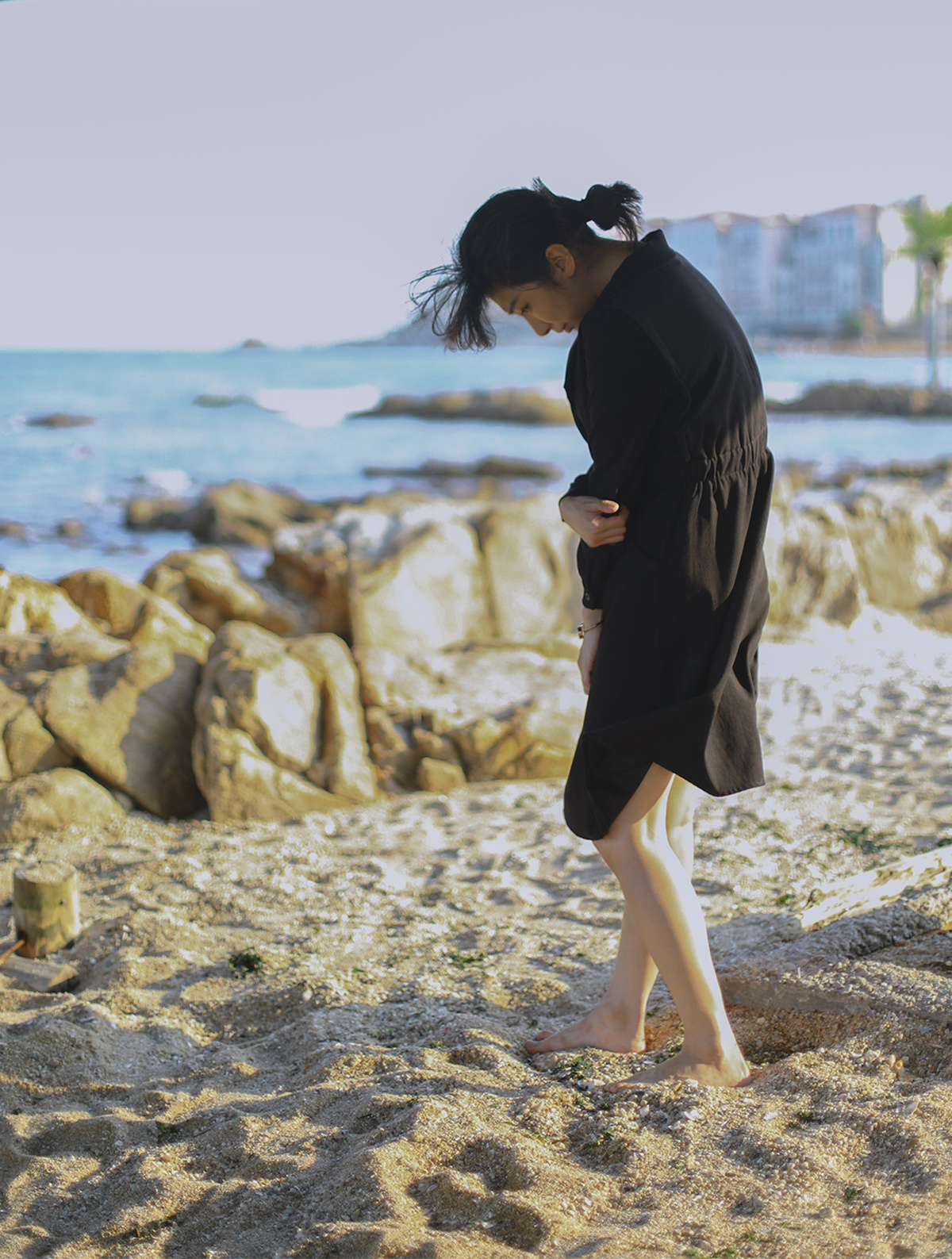 一个穿黑色衣服的年轻女子正在沿着岩石海滩走 而另一个人站在沙滩上。