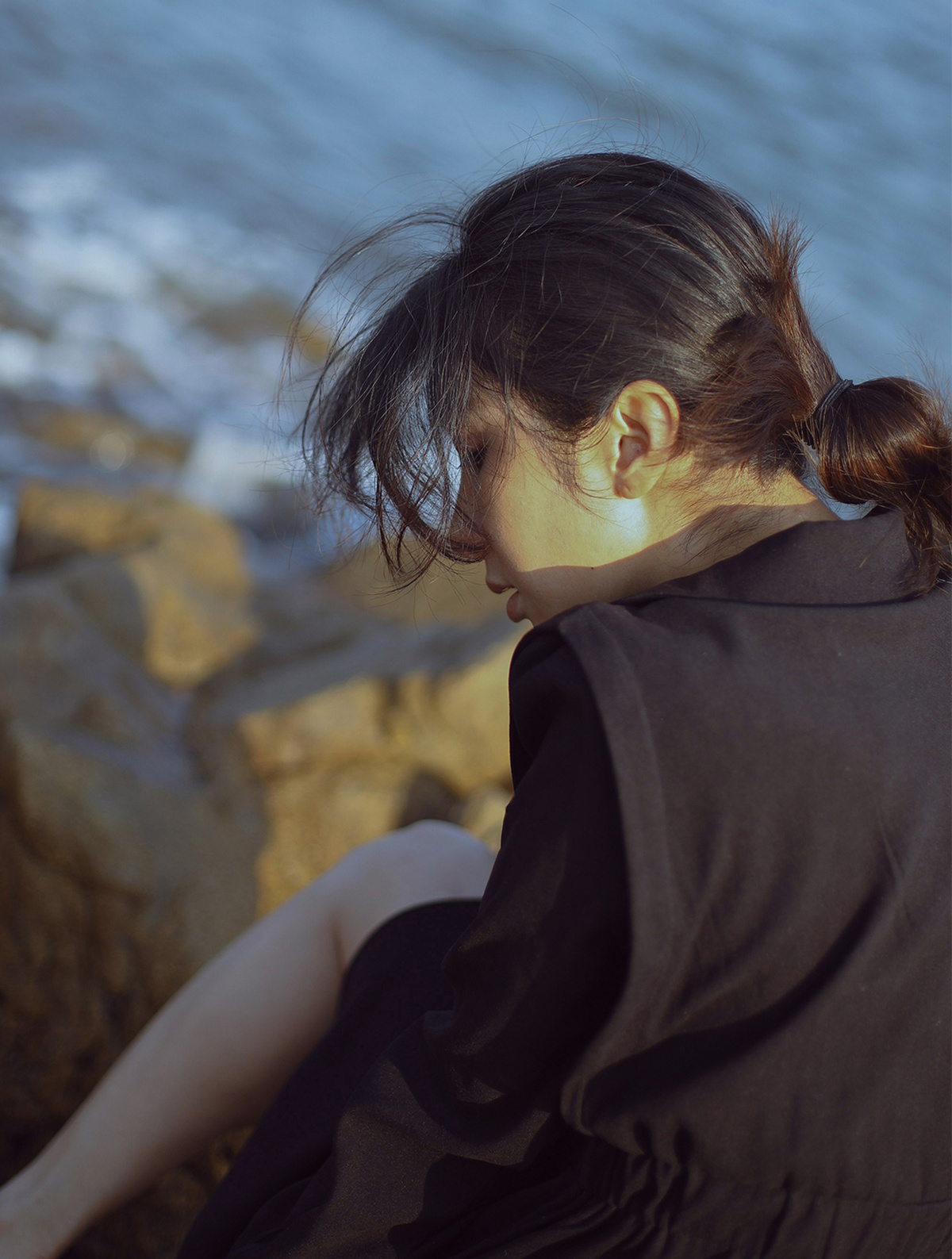 一个穿着黑色连衣裙的年轻女子坐在岩石上 眺望着海洋。