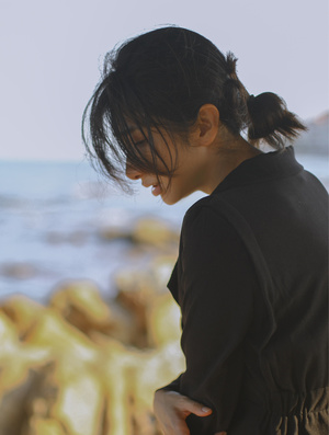 一位年轻女子站在海滩上 背景中有水和岩石 正在看手机。