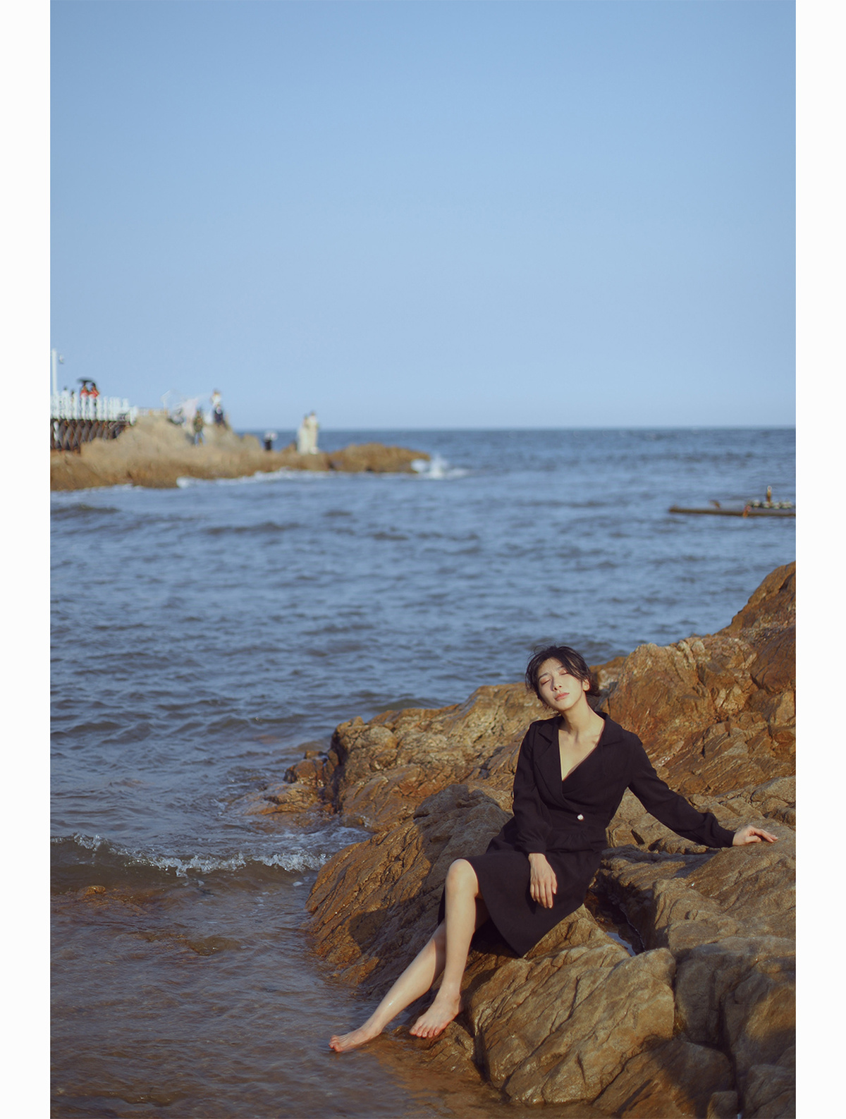 一个穿着黑色连衣裙的女人坐在海边的一些岩石上