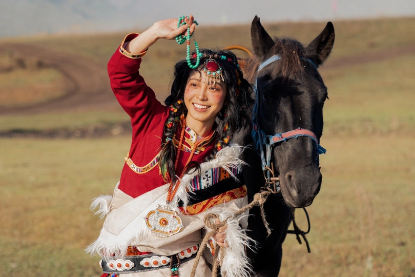 一位穿着传统服装的年轻女子站在一匹黑马旁边。