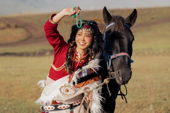 一位穿着传统服装的年轻女子站在一匹黑马旁边。