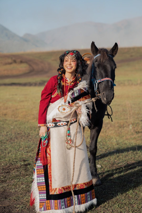 一位穿着传统服装的年轻女子站在一匹黑马旁边。