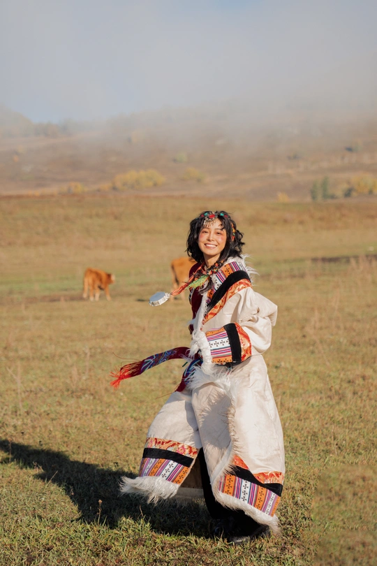 一位穿着传统服装的年轻女子站在草地上 背景中有牛。