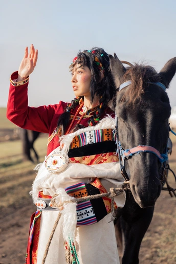 一位穿着传统印度服装的年轻女子站在一匹黑马旁边的一个田野中。