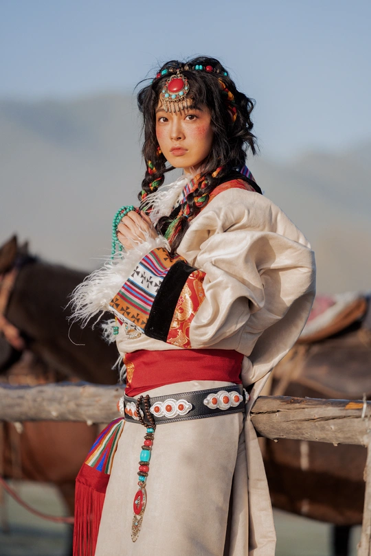 一位穿着传统印度服装的年轻女子站在围栏前 背景中有一匹马。