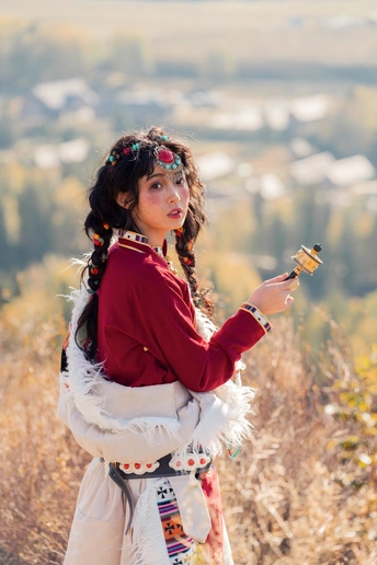 一位身着传统服装的年轻女子站在一个俯瞰着田野的山丘上 背景中有一座山。