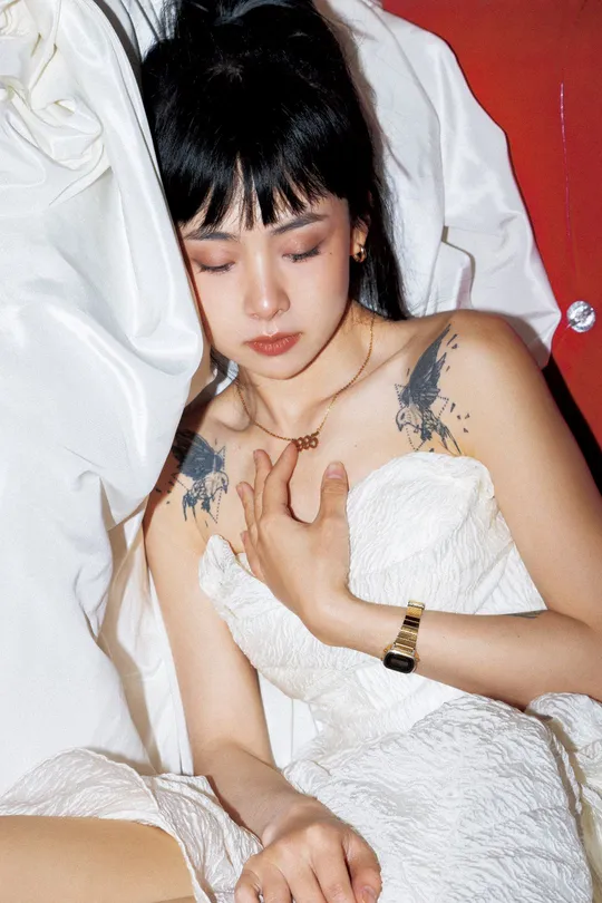 一个有纹身的年轻女子坐在一张白色床上