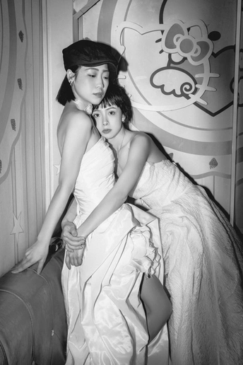 一张黑白照片 一位年轻女士穿着连衣裙和帽子 坐在箱子旁边。