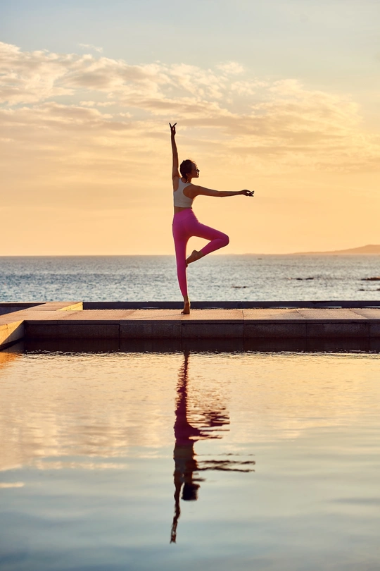 夕阳下在海滩边练习瑜伽的年轻女子