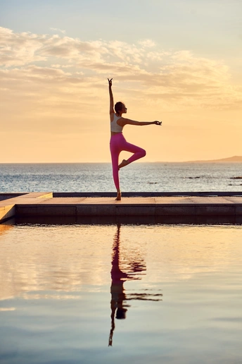 夕阳下在海滩边练习瑜伽的年轻女子