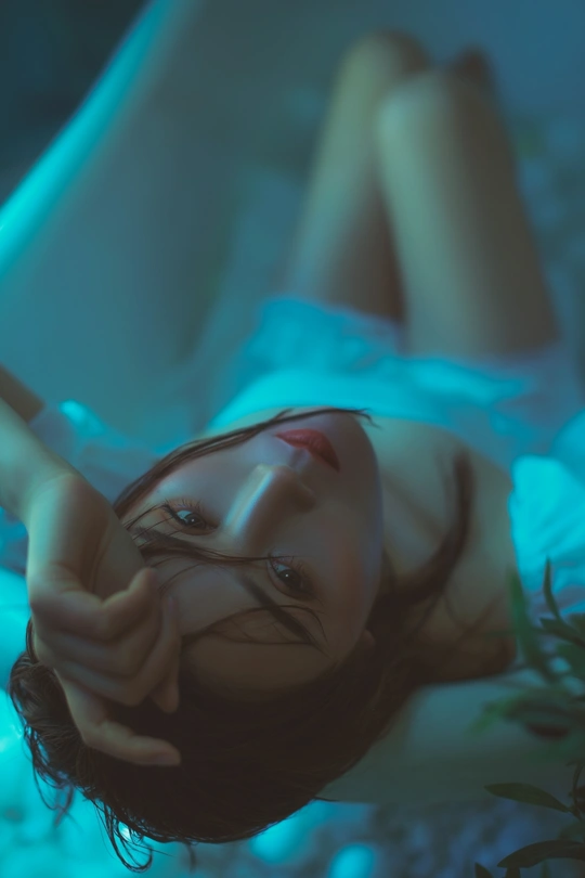 一位女性躺在蓝色的灯光照射的水坑中的床上。
