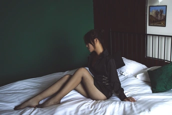 一个穿黑色长筒袜的年轻女子坐在一张白色床上